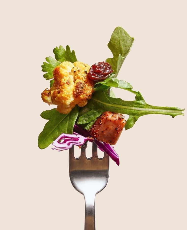 Tenedor con un bocado de coliflor asada, arúgula, proteína y col morada