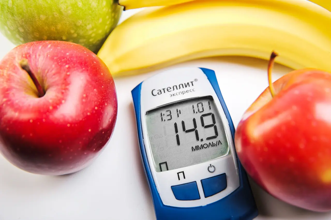 Glucómetro mostrando una lectura de glucosa junto a manzanas y plátanos